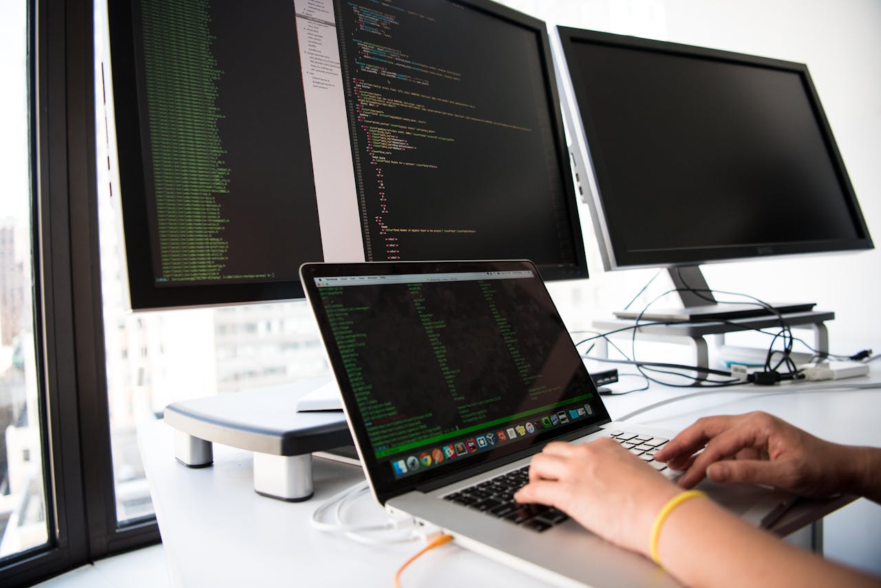 menu-17 A developer writes code on a laptop in front of multiple monitors in an office setting.