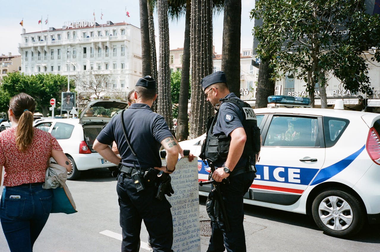 menu-14 Police officers and a civilian interact near a police car on a busy city street.