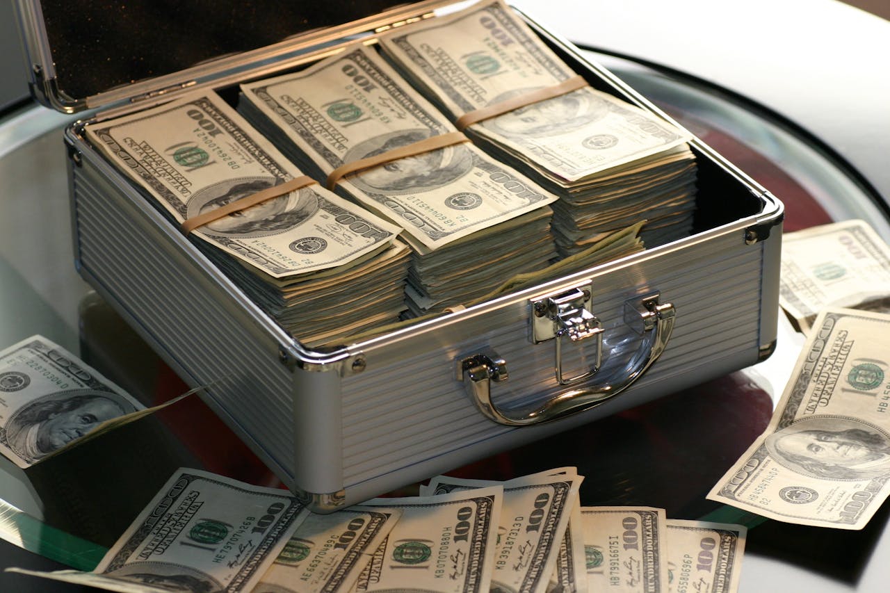 menu-08 Open briefcase filled with stacks of hundred dollar bills on a glass table, representing wealth.